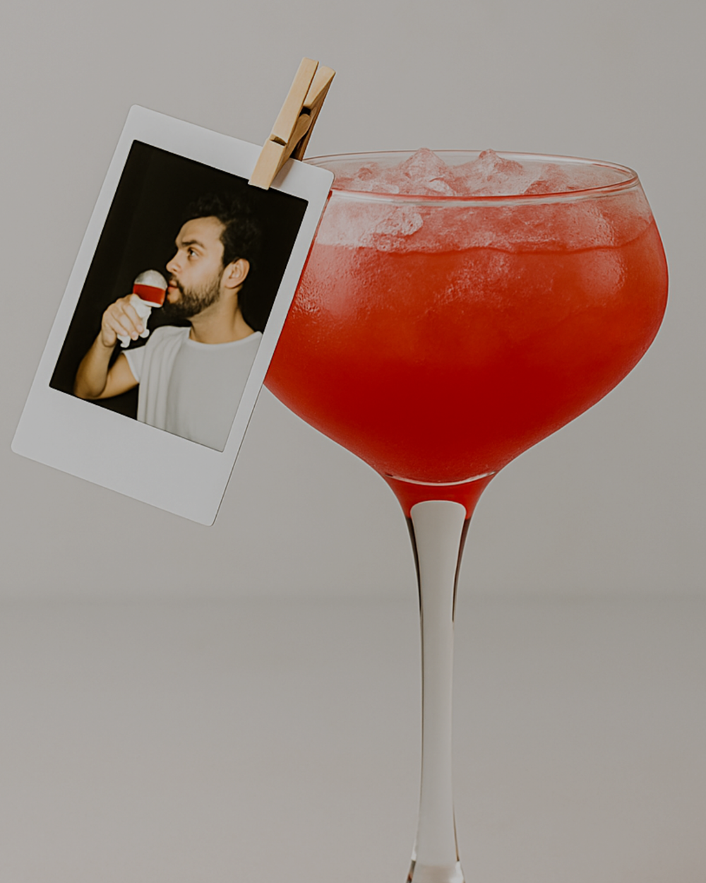Girls on Film, a red cocktail over ice in a stemmed glass with a miniature photograph clipped to the rim.