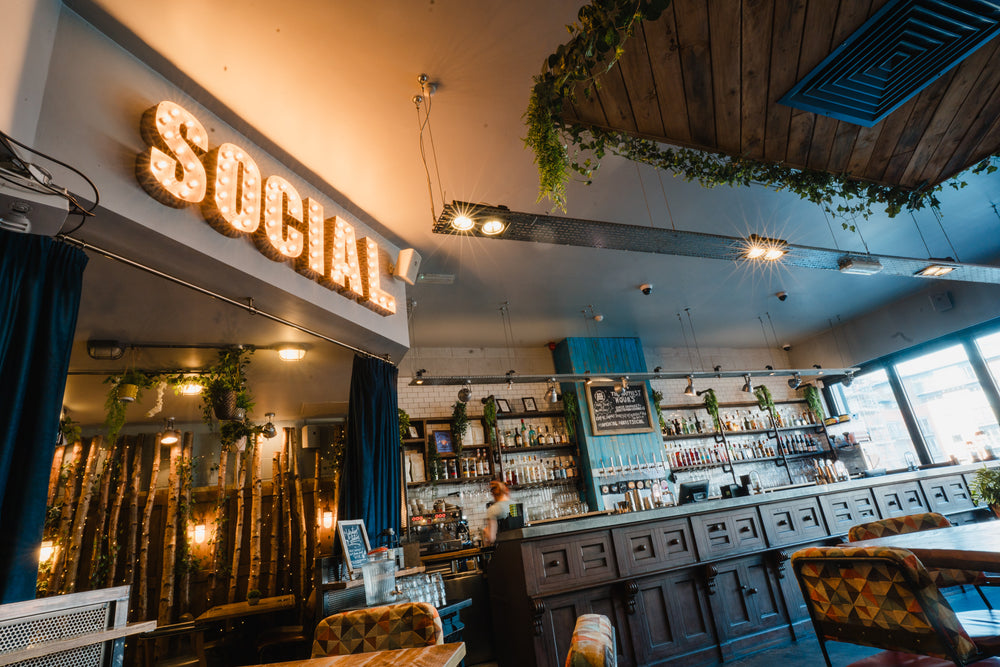 Gas Street Social cocktail bar at The Mailbox in Birmingham, featuring an illuminated SOCIAL sign, extensive bottle displays, dark wooden bar and contemporary industrial interiors.