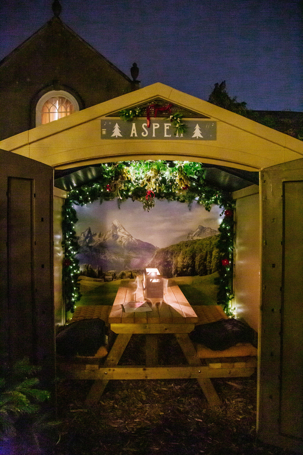 Festive Christmas chalet with illuminated garlands, Christmas decorations and cosy wooden seating, creating a warm alpine-inspired dining experience.