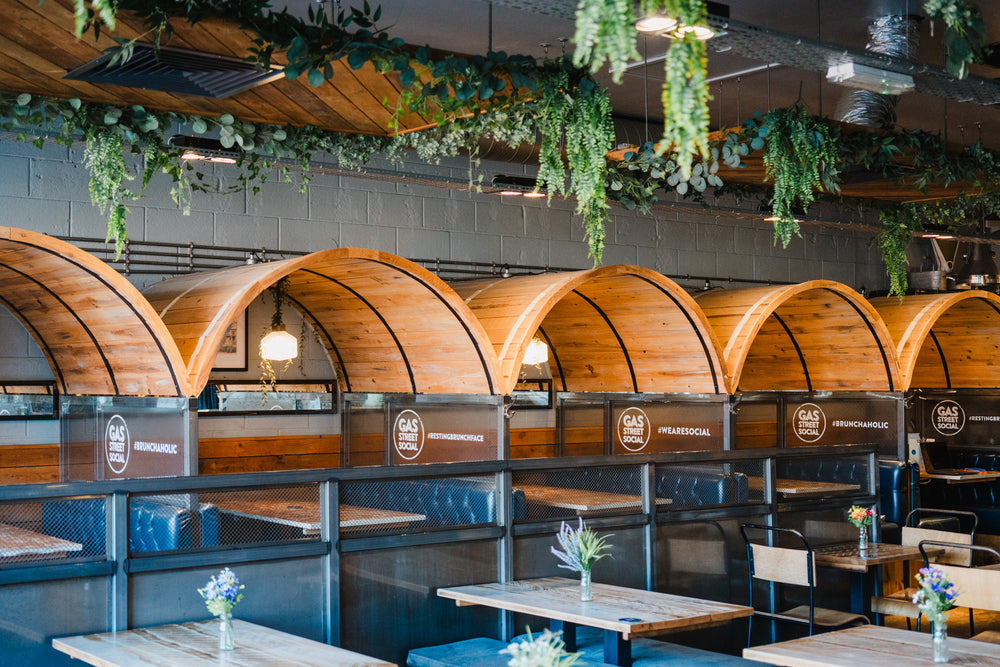 Wooden booth seating with blue upholstery and hanging greenery inside Gas Street Social restaurant and cocktail bar at The Mailbox in Birmingham.