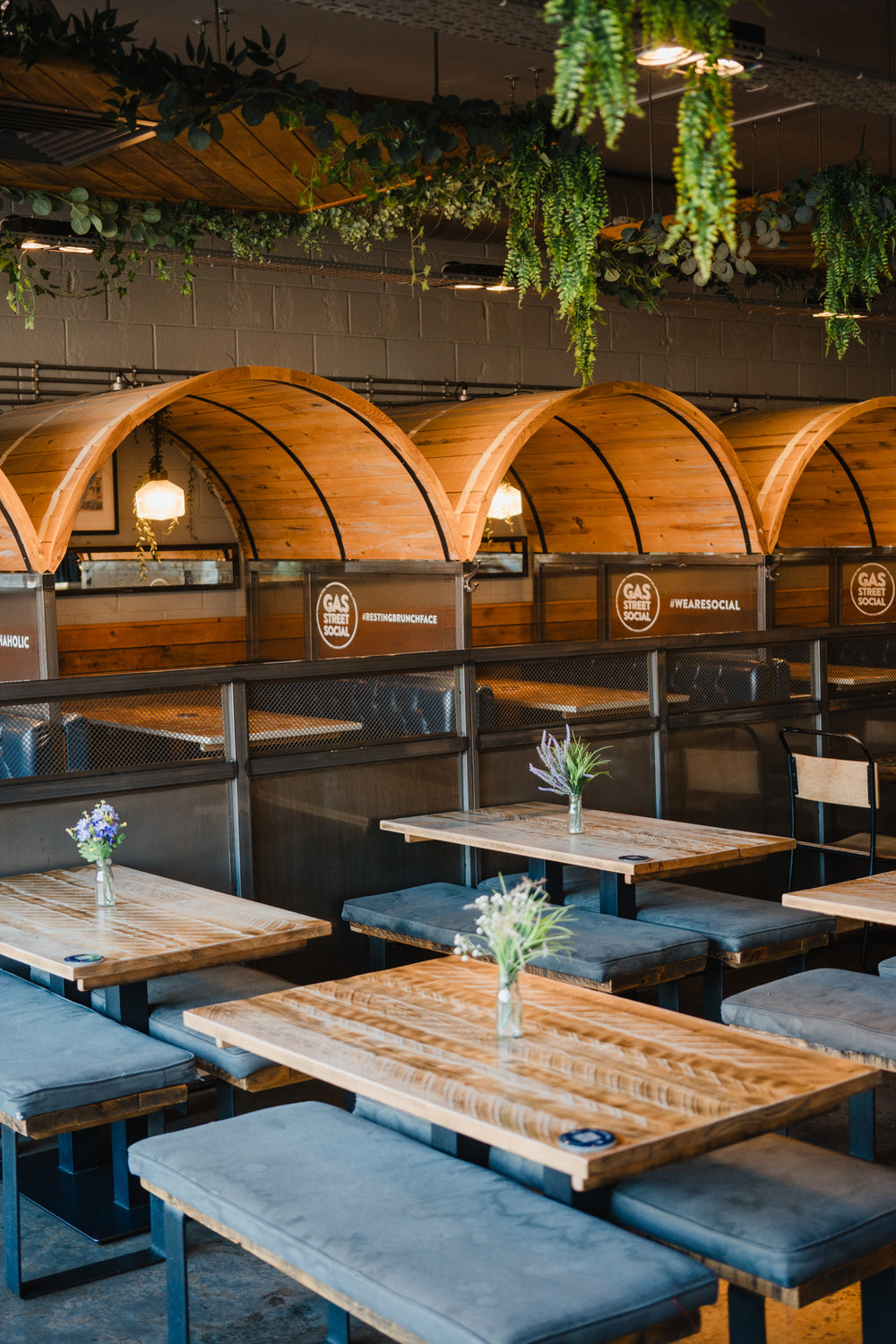 Wooden booth seating, communal dining tables and hanging greenery inside Gas Street Social restaurant and cocktail bar at The Mailbox, Birmingham.
