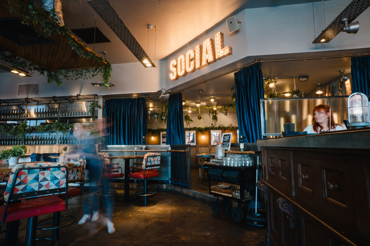 Interior of Gas Street Social at The Mailbox in Birmingham, featuring colourful booth seating, hanging greenery and illuminated SOCIAL signage.